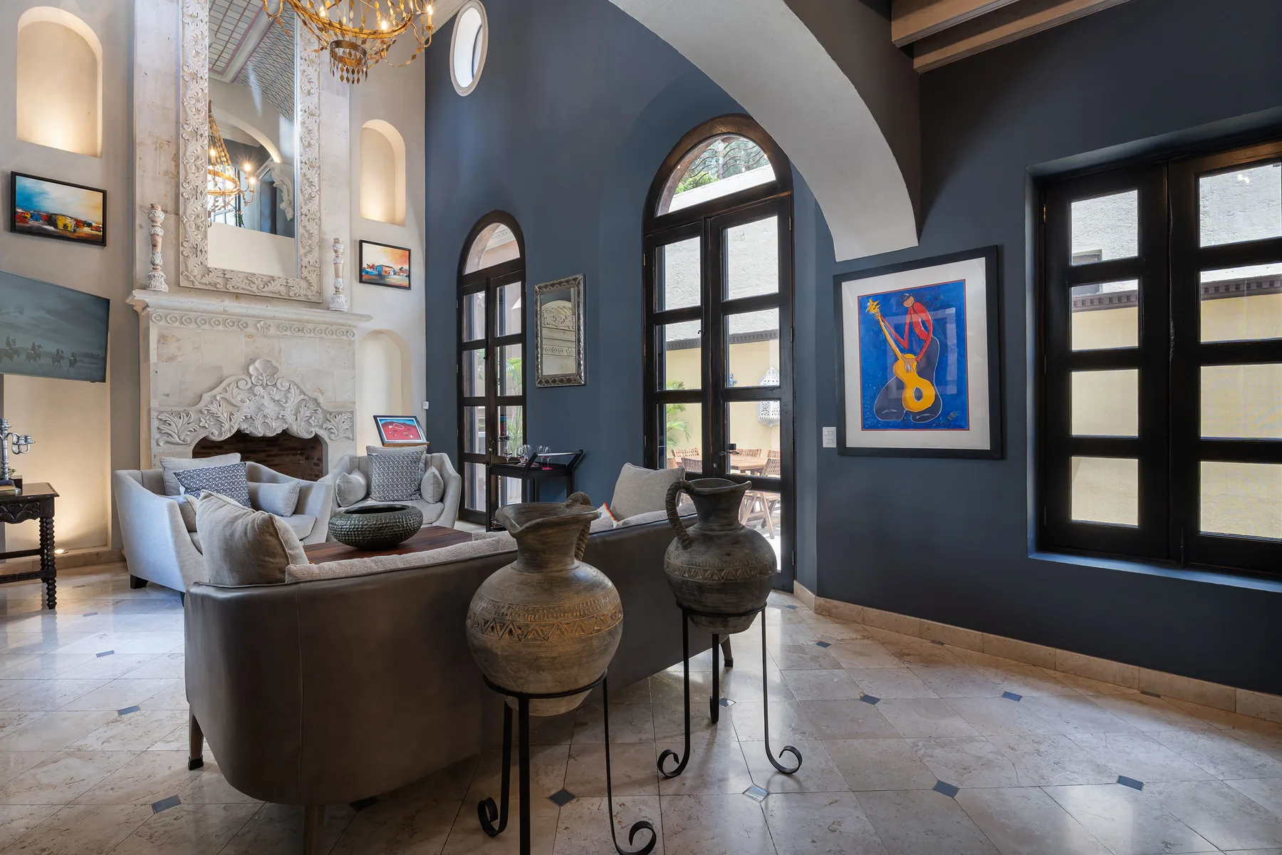 A high-ceilinged living room with seating, arched windows, and framed artwork.