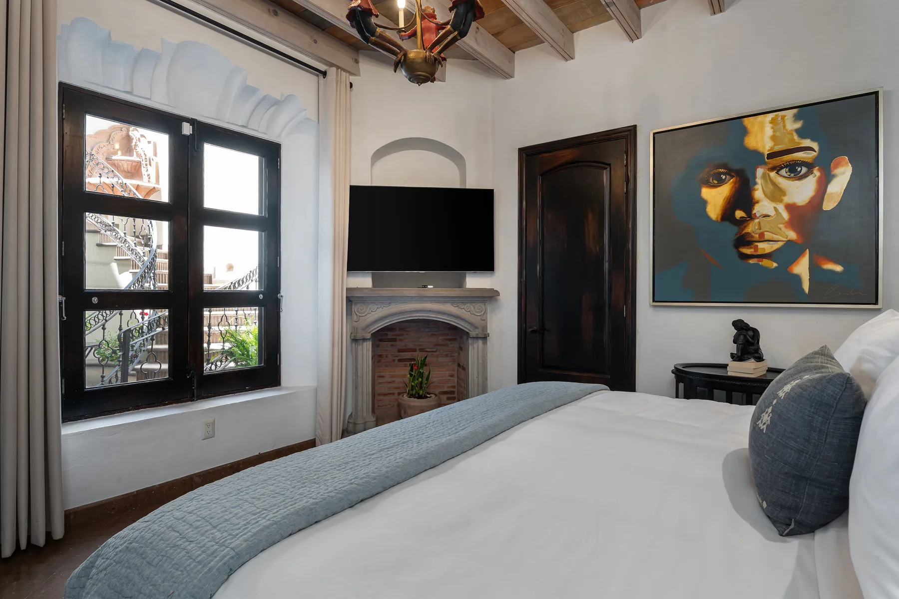 A bedroom with a large bed, a window, and a fireplace beneath a television.