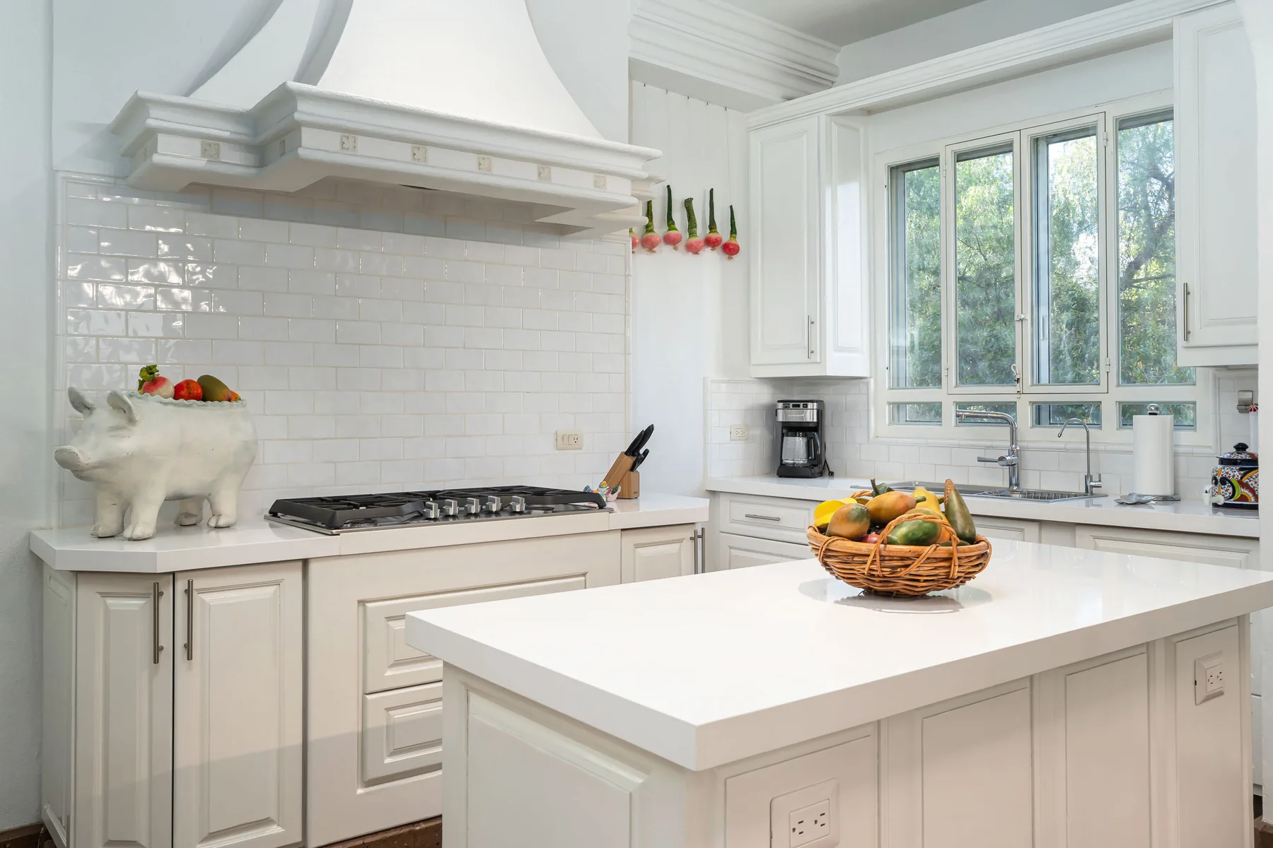 A bright white kitchen with a large island and a window overlooking greenery.