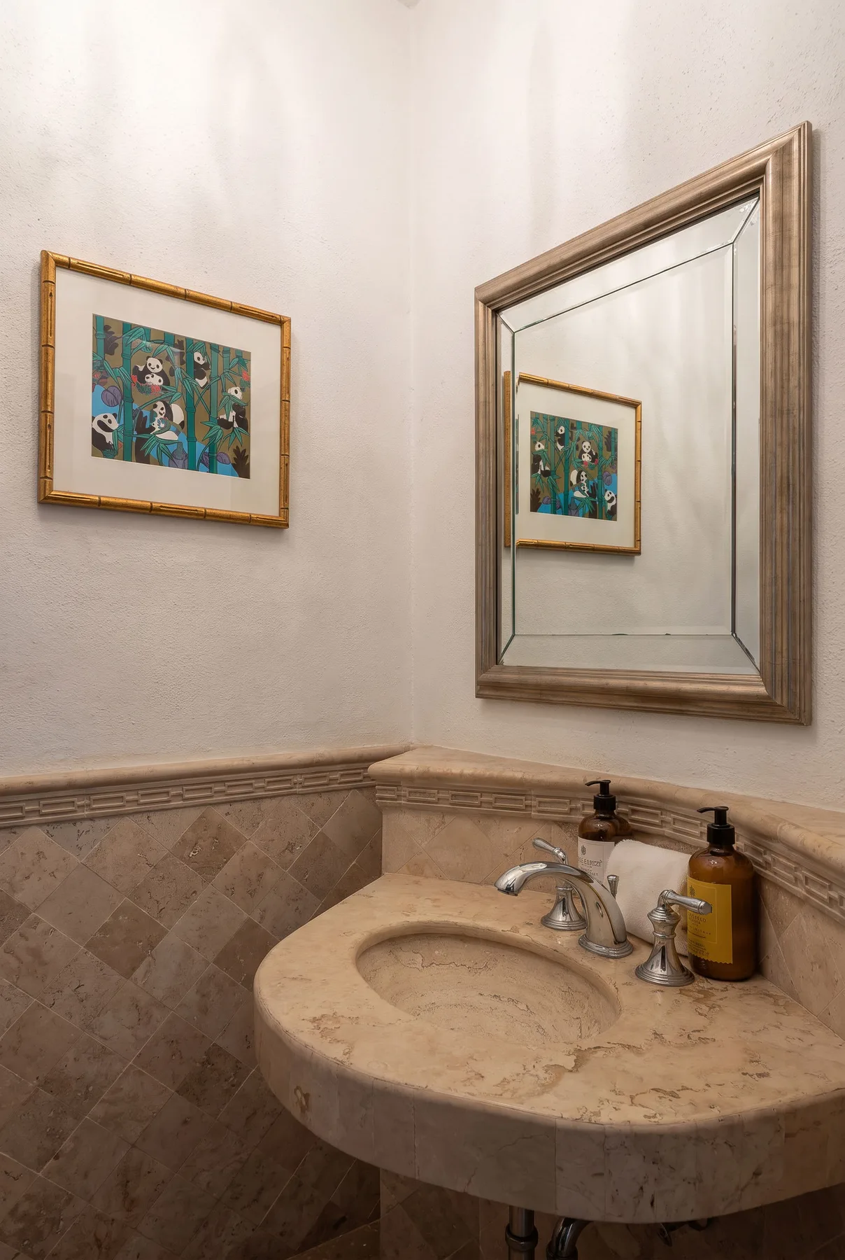 A bathroom sink sits beneath a large wall mirror, with framed artwork nearby.