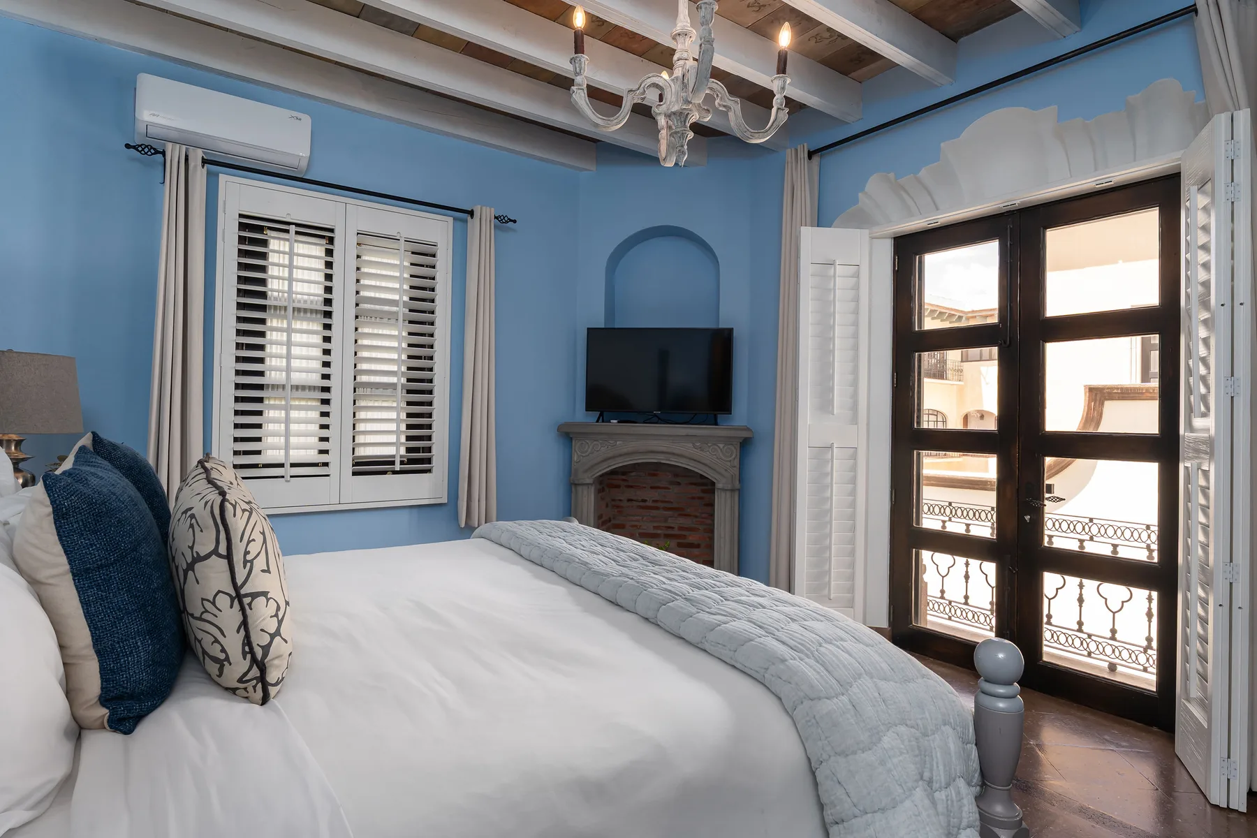 A blue bedroom with a bed, a television, and an open balcony doorway.