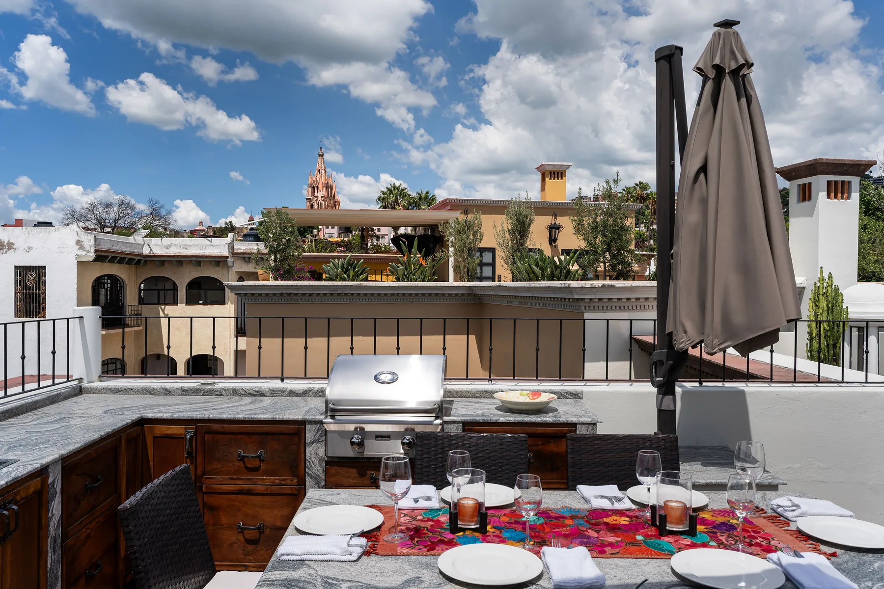 A rooftop dining and barbecue area has a set table and a closed patio umbrella.