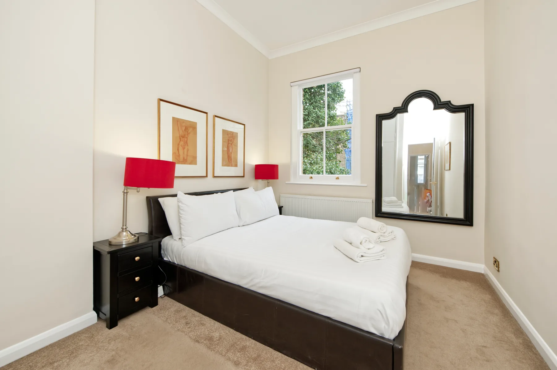 Un dormitorio luminoso con una cama bien tendida bajo cuadros enmarcados.