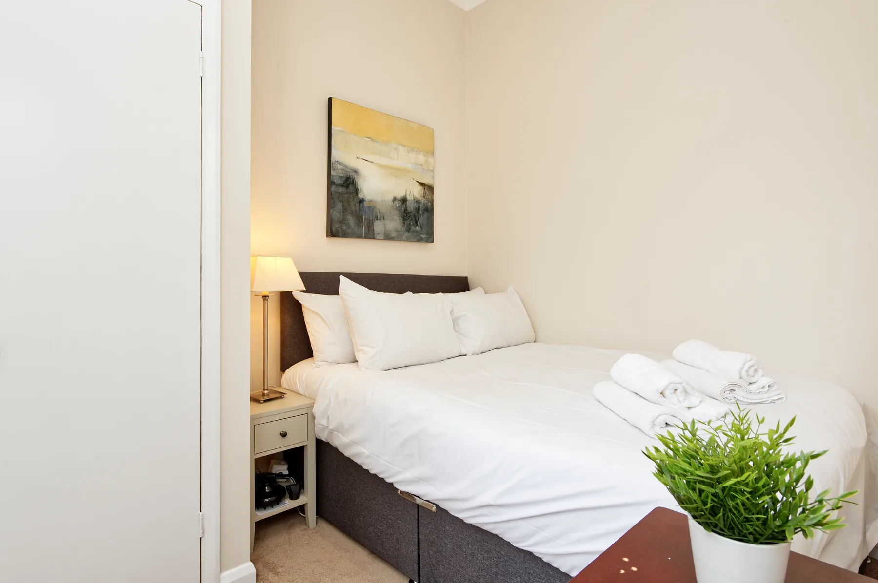 Un dormitorio con una cama tendida, ropa de cama blanca y una lámpara de noche.