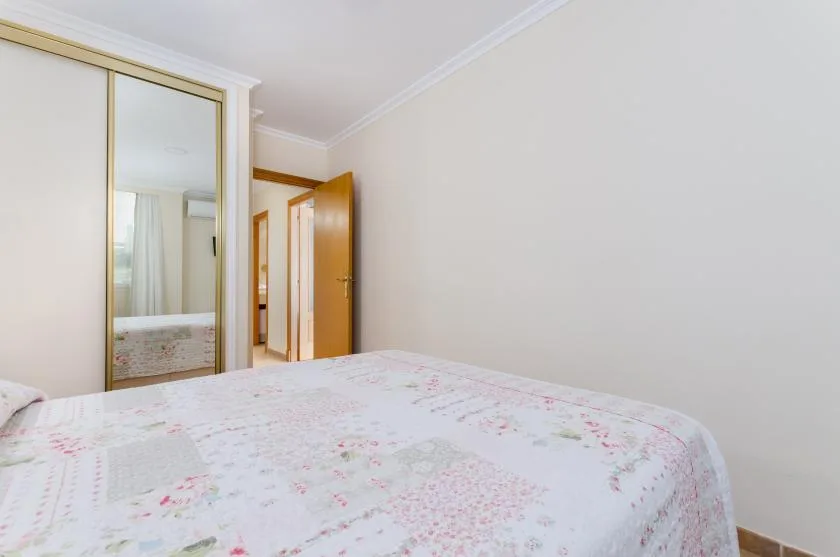 A bedroom with a floral bedspread and a mirrored wardrobe.