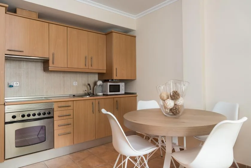 Una zona de cocina y comedor con armarios de madera, horno y mesa redonda.