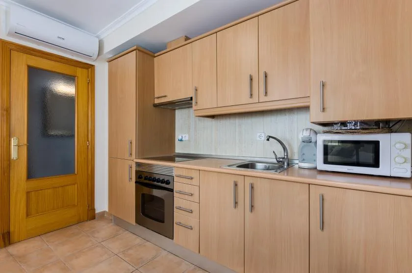 A kitchen with light wood cabinets, a sink, and a microwave.
