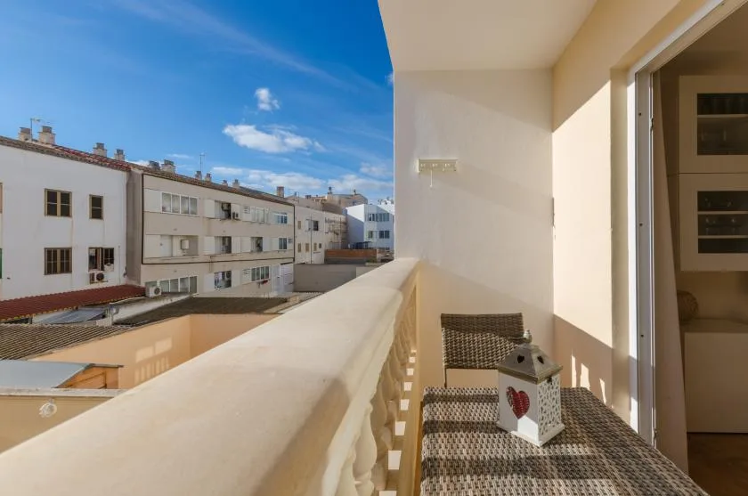 A sunlit balcony overlooks neighboring buildings, with a small table and chair.