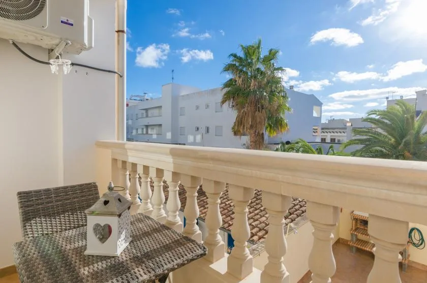 A balcony with wicker seating overlooks nearby buildings and palm trees.