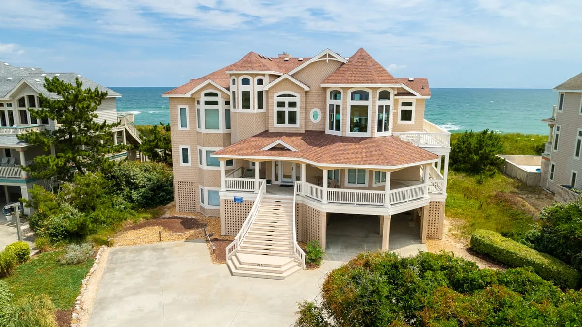 A large coastal house stands beside the ocean, with a broad staircase leading to its entrance.