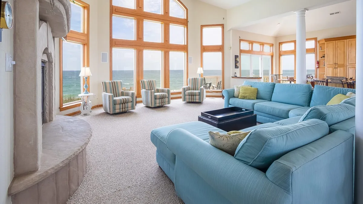 A bright living room with blue seating and large windows overlooking the water.