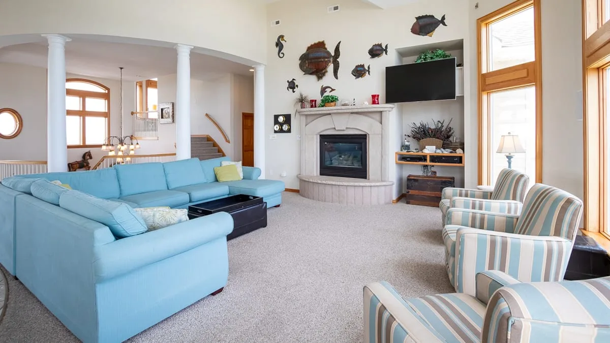 A bright living room with blue seating, a fireplace, and tall windows.