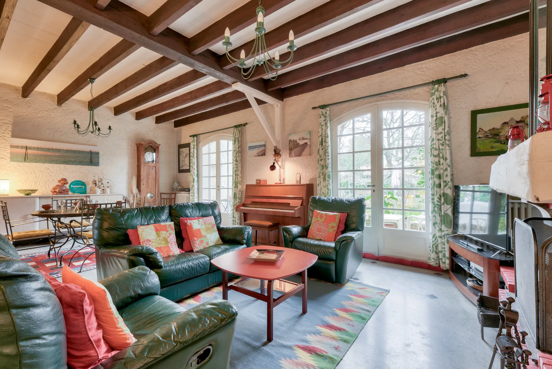 A living room with green seating, a piano, and large windows.