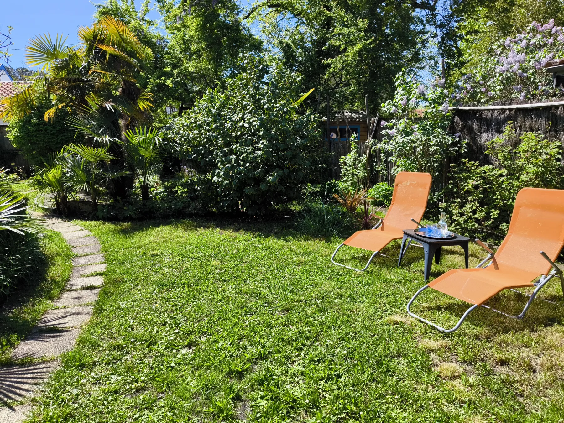 A leafy garden seating area with orange loungers and a small table.