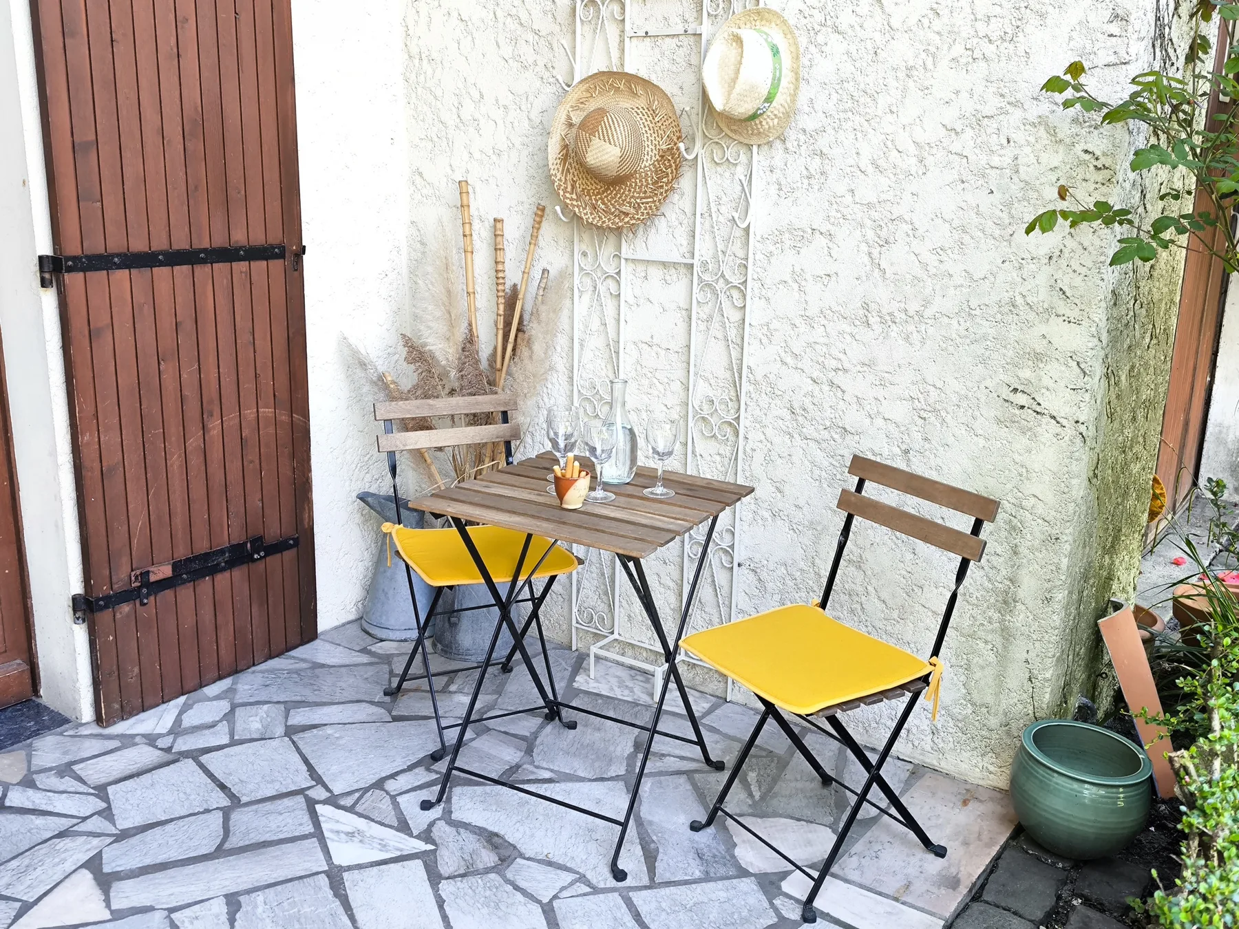 A small outdoor dining area has a table, yellow seating, and potted plants.