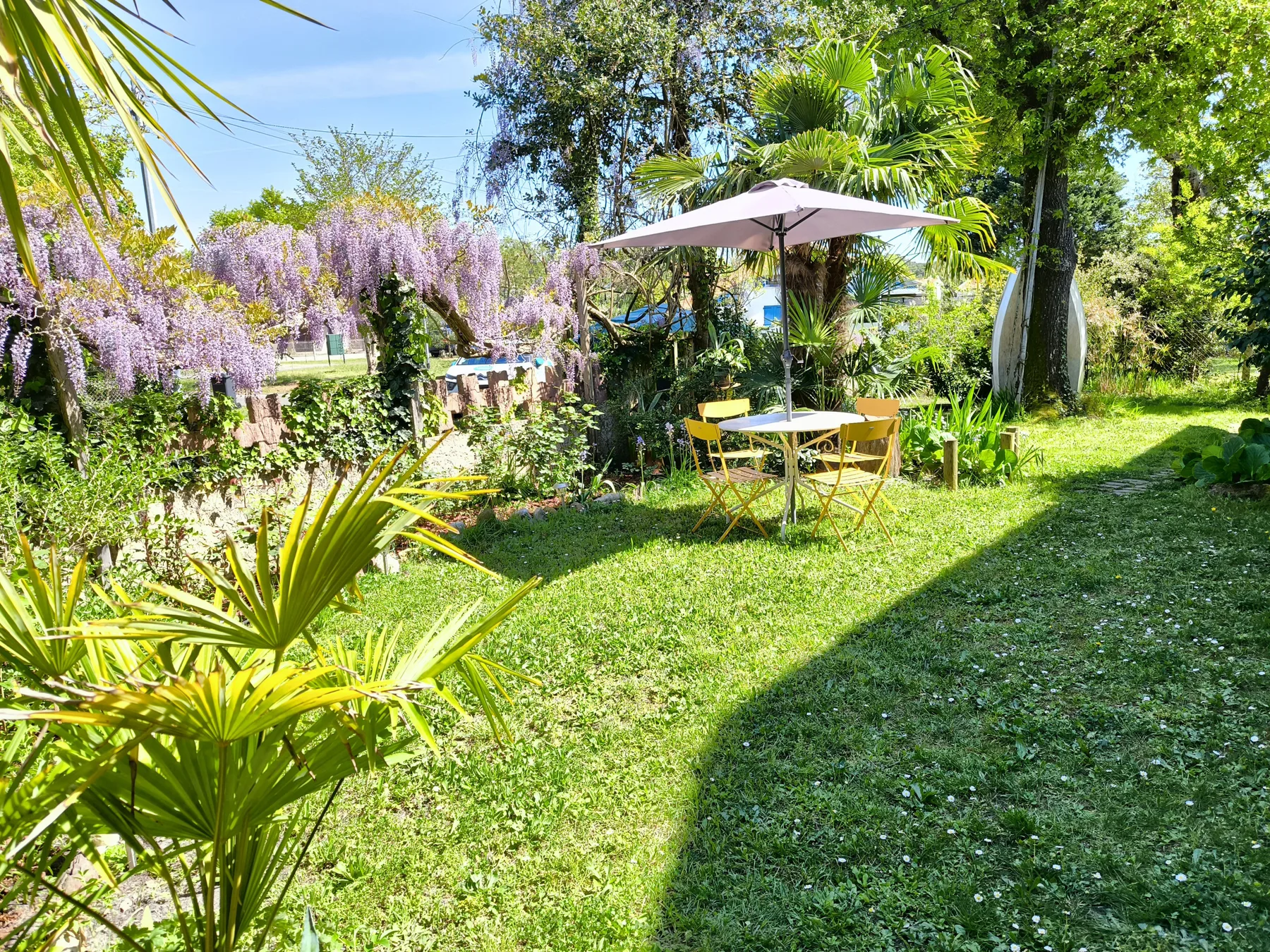 A garden seating area with a table and umbrella amid lush greenery.