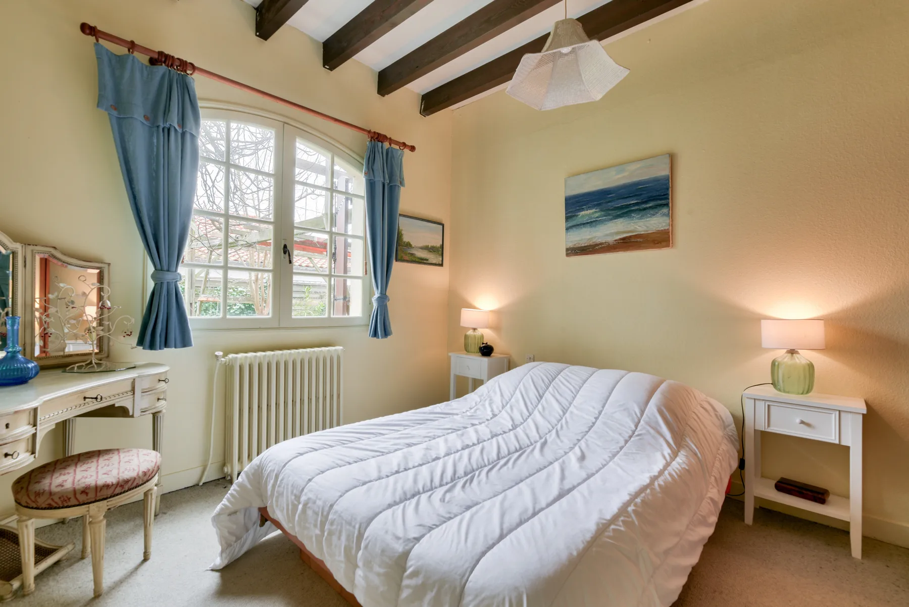 A bedroom with a bed beneath a large window and framed artwork on the walls.