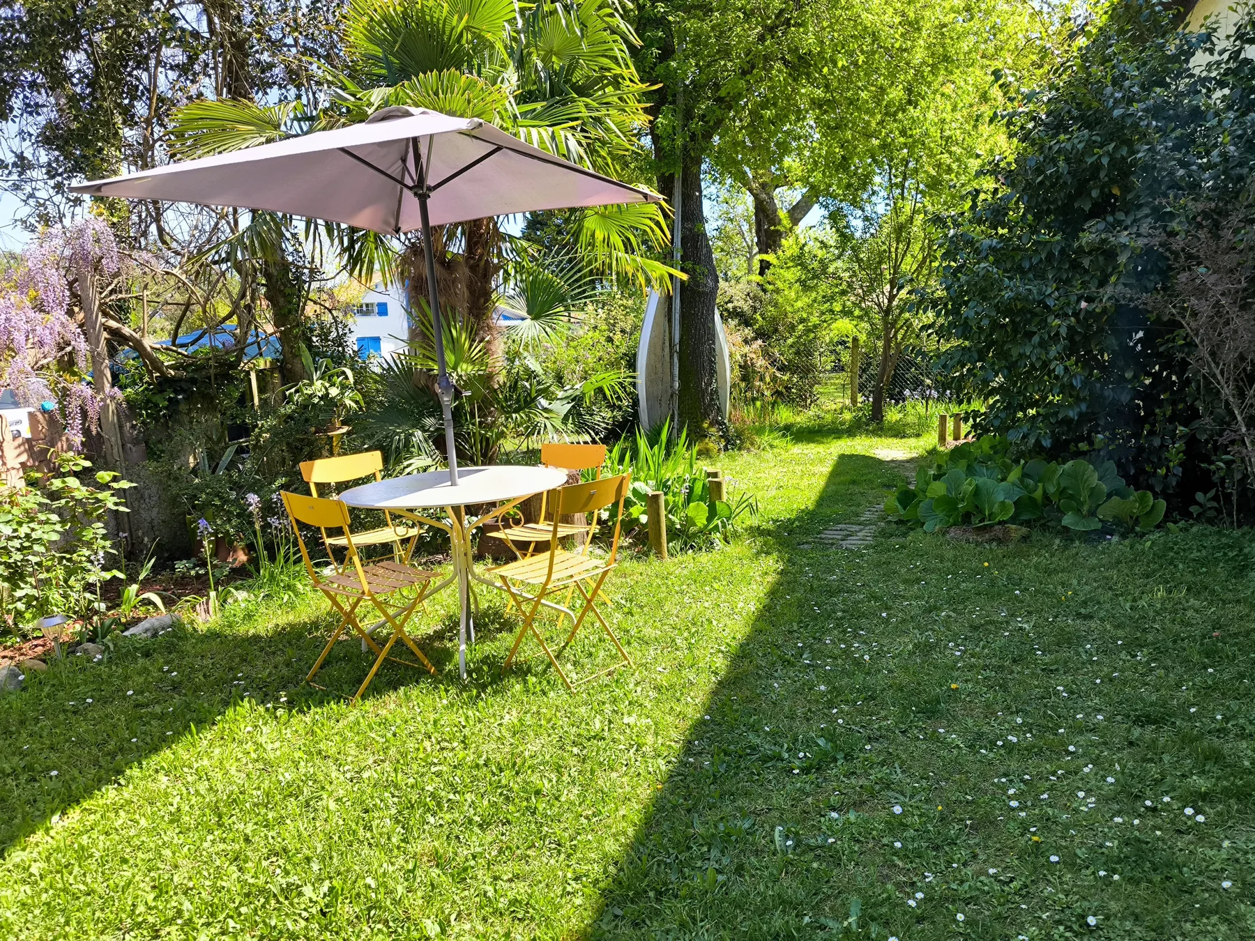A garden seating area with a table and umbrella sits beside a grassy path.