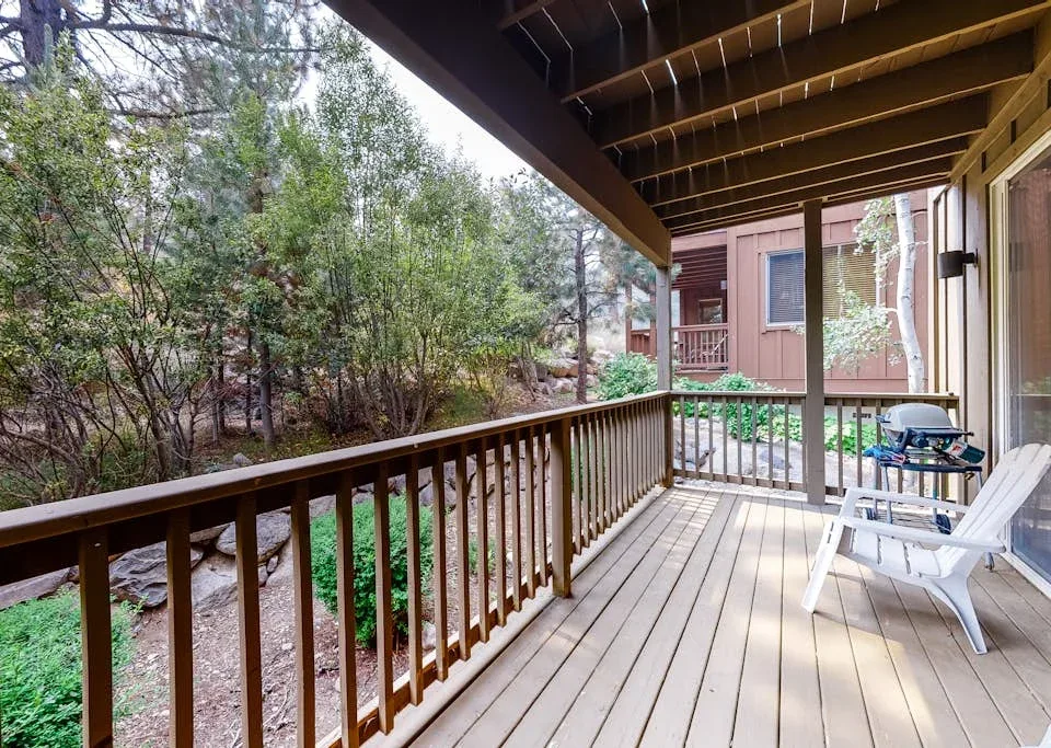 A covered wooden deck overlooks leafy shrubs and trees.