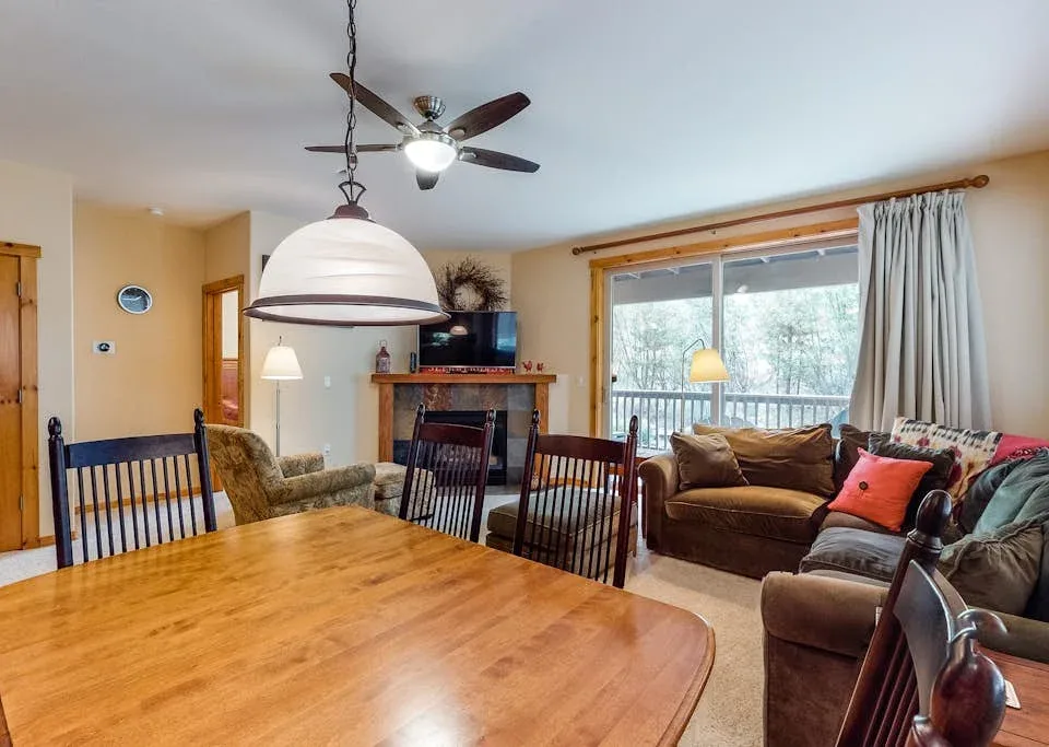 A dining area opens onto a living room with seating and large windows.