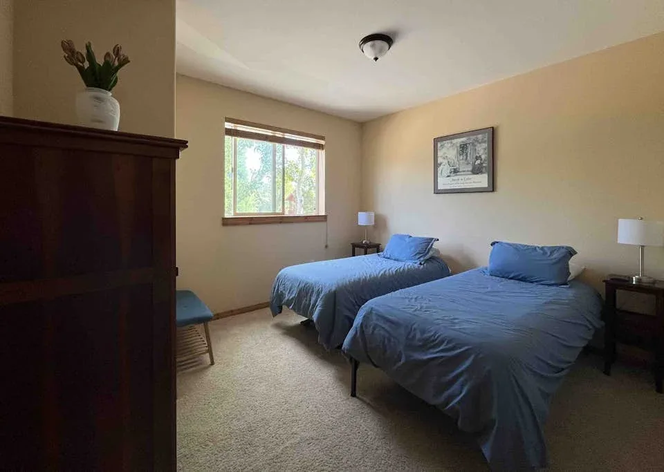 A bedroom with two beds covered in blue bedding and a window.