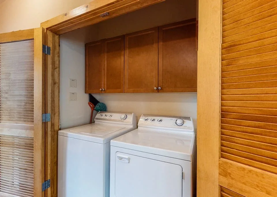 A laundry area with a washer and dryer beneath wooden cabinets.