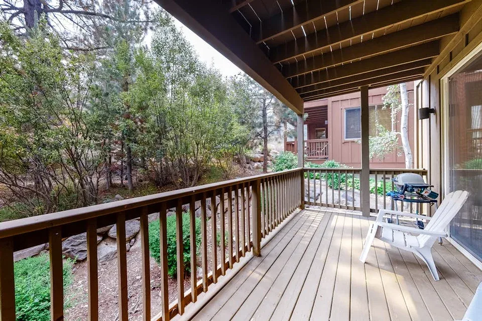 A covered wooden deck with outdoor seating overlooks a wooded area.