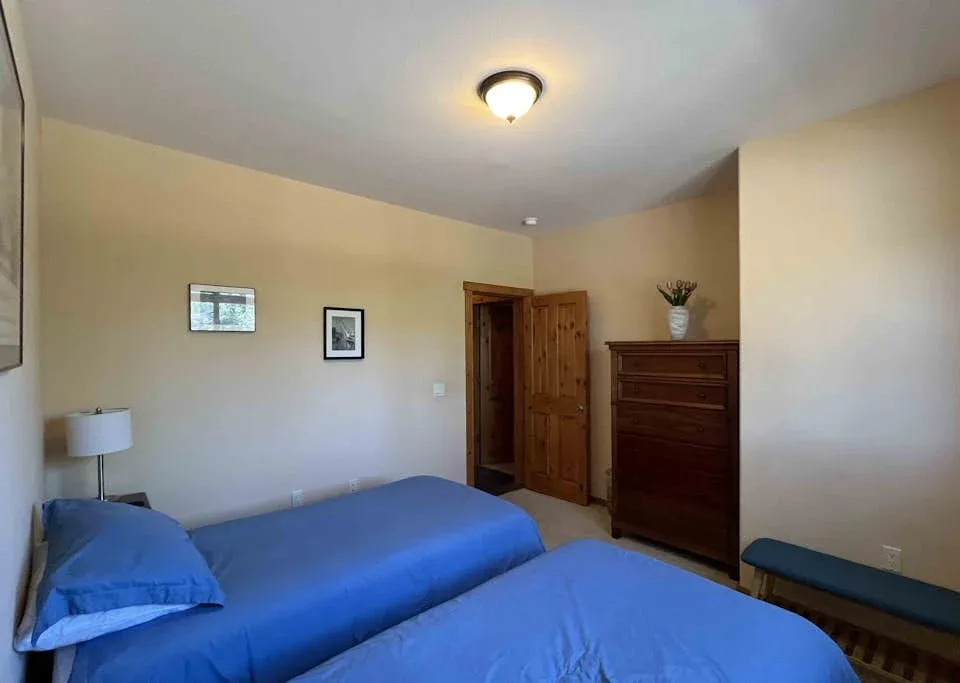 A bedroom with blue bedding, a wooden dresser, and an open doorway.