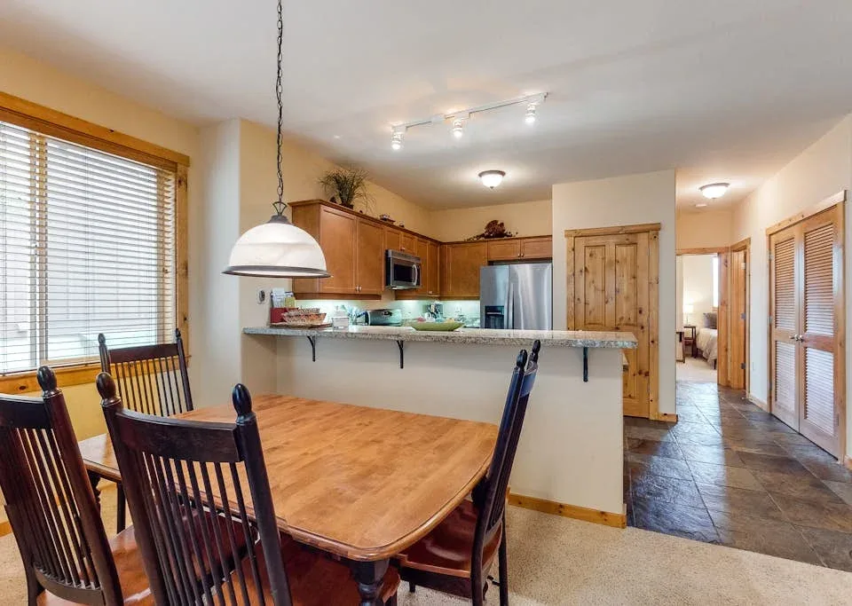 A dining area opens onto a kitchen, with a wooden table beside the counter.