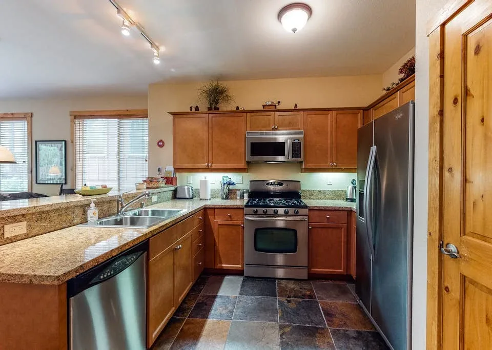 A kitchen with wooden cabinets, stone counters, and stainless steel appliances.