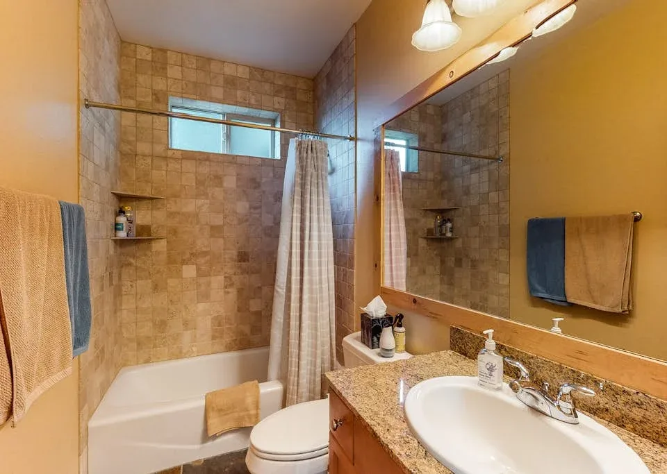 A bathroom with a tiled bathtub, shower curtain, and sink.