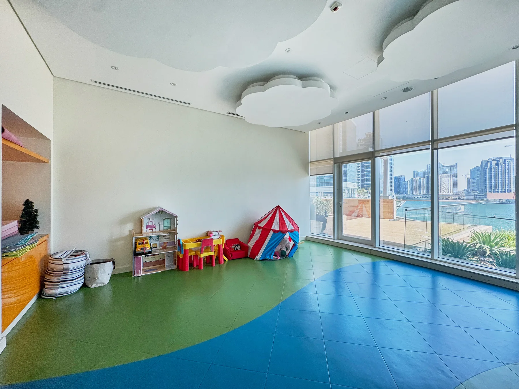 Zona común: Una colorida sala de juegos interior con juguetes y grandes ventanales con vistas a la ciudad.
