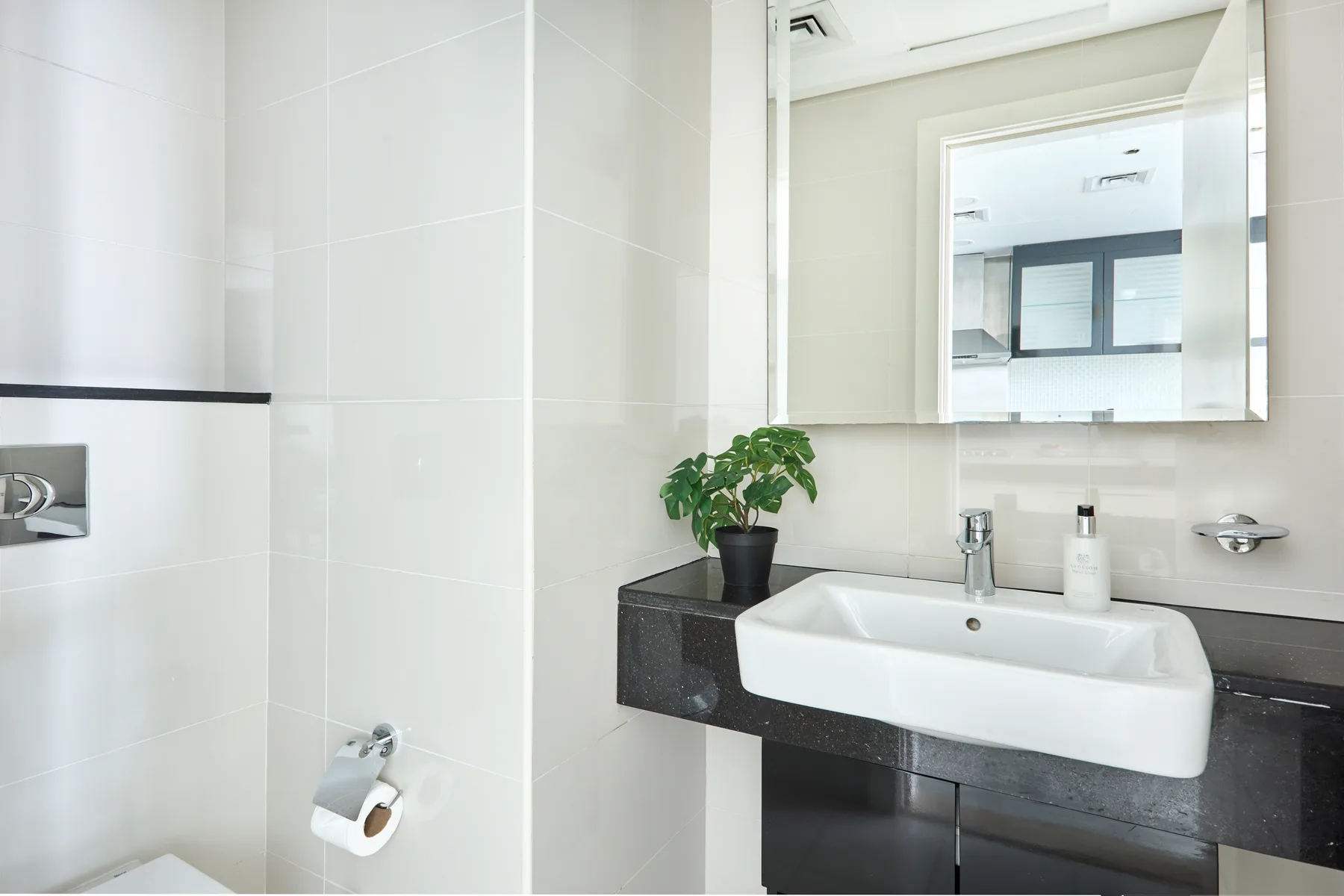 Un baño con azulejos, un lavabo blanco, una encimera oscura y un espejo.