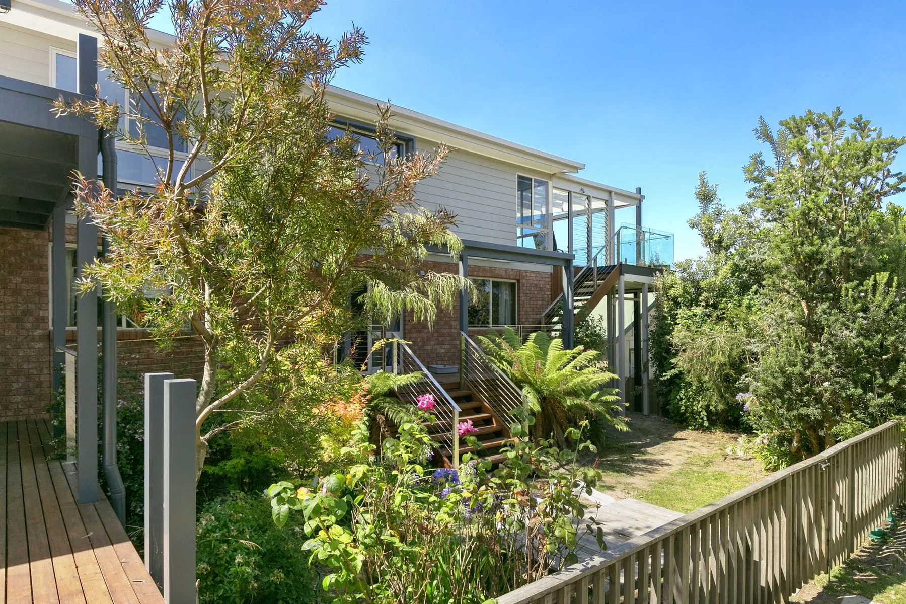 A landscaped garden beside a modern house with an elevated deck and stairs.
