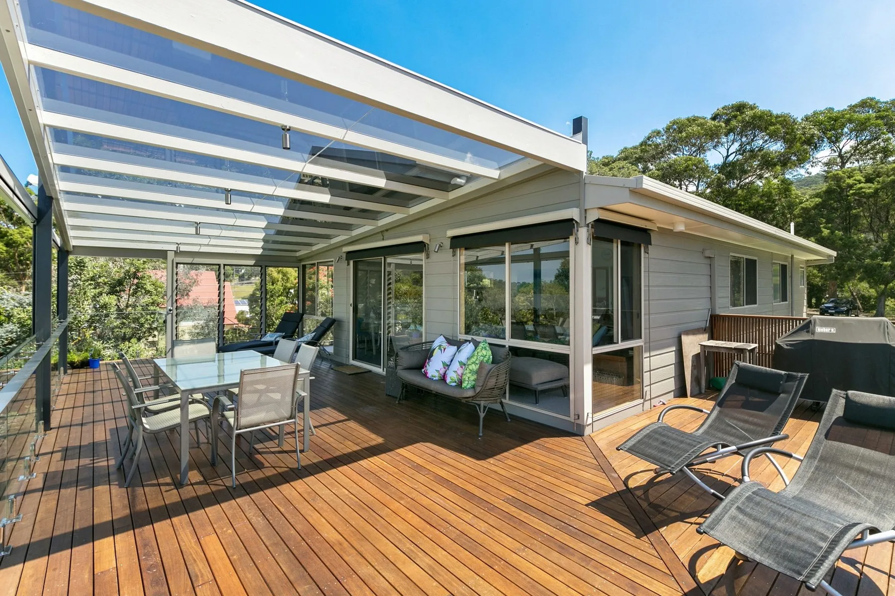 A covered outdoor deck with seating and large windows overlooks surrounding trees.