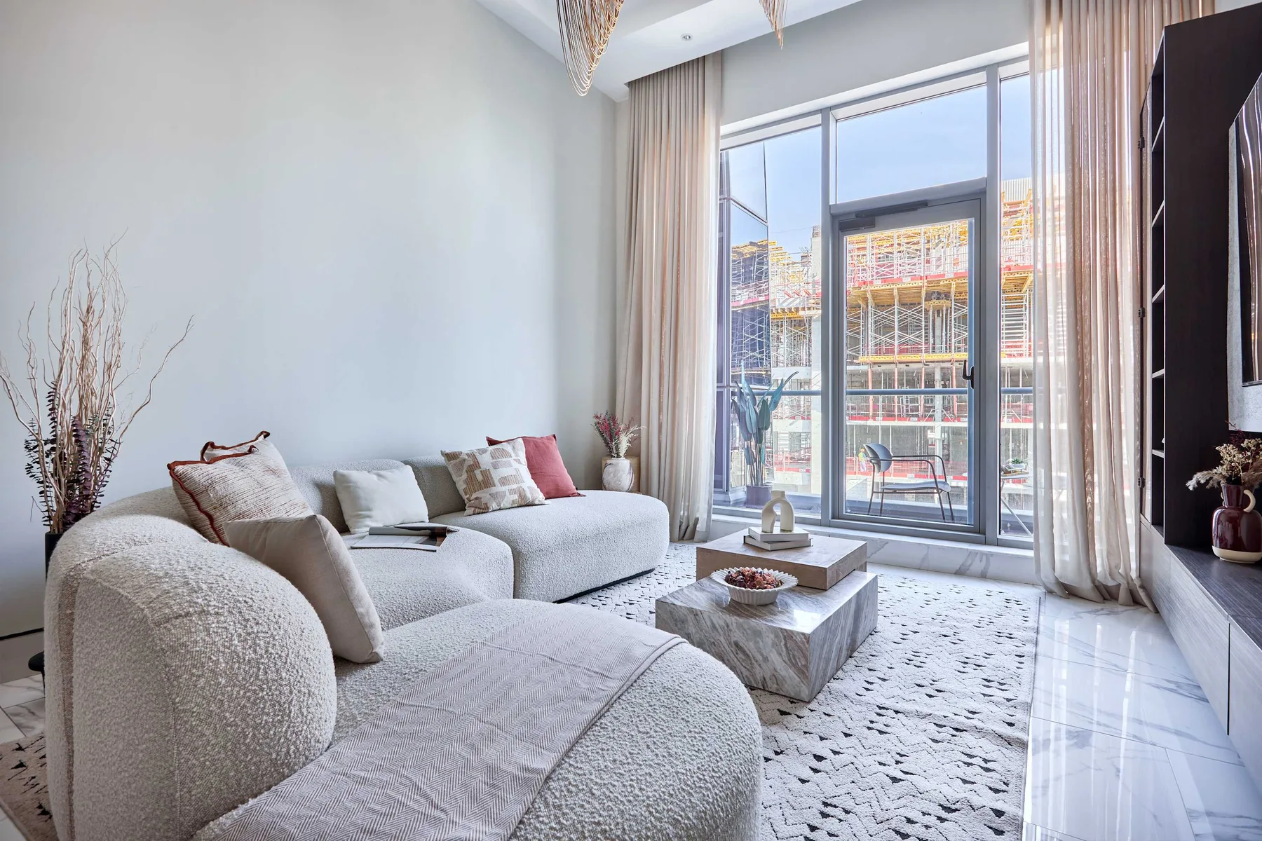 A bright living room with pale seating and large glass doors opening onto a balcony.