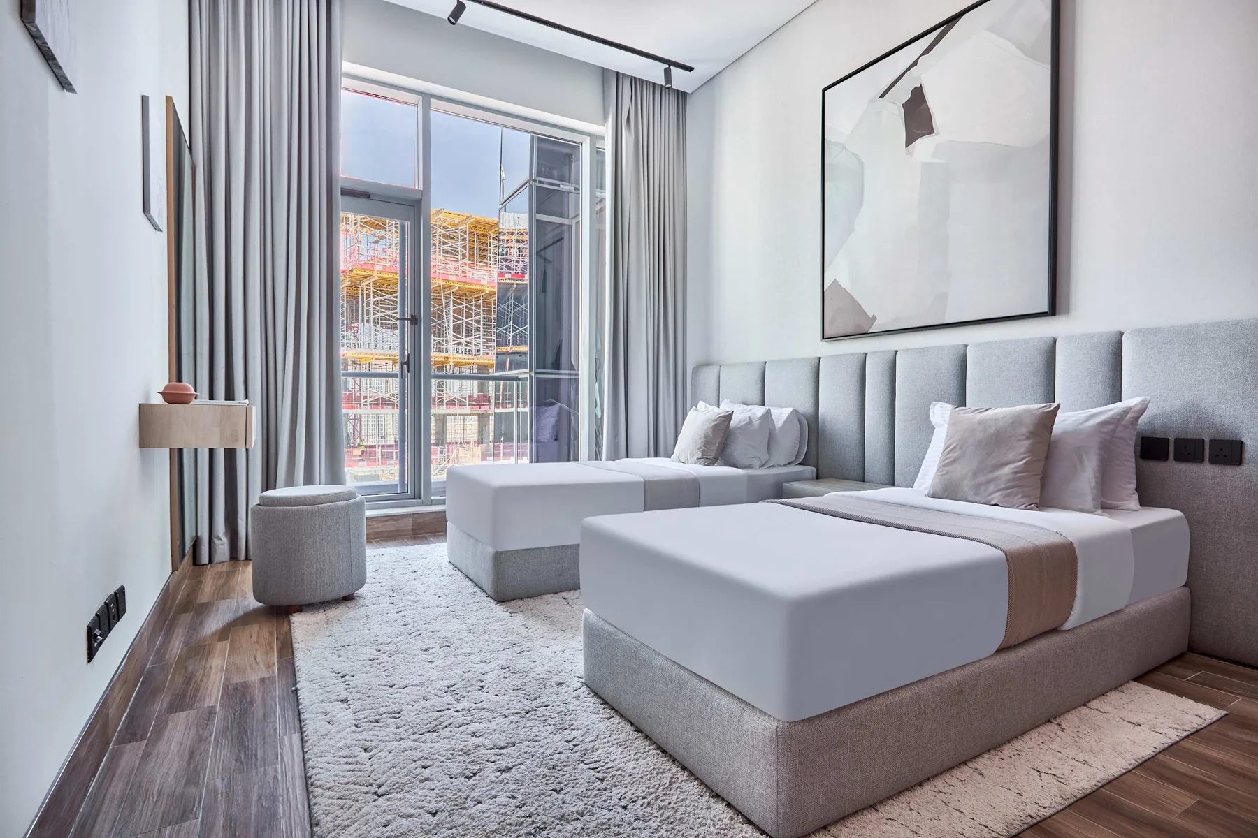 A modern bedroom with two beds and a large window overlooking nearby buildings.