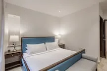 Un dormitorio con una cama azul, ropa de cama blanca y mesitas de noche.