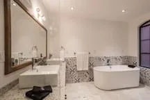 Un baño con una bañera exenta, un lavabo y paredes de azulejos estampados.
