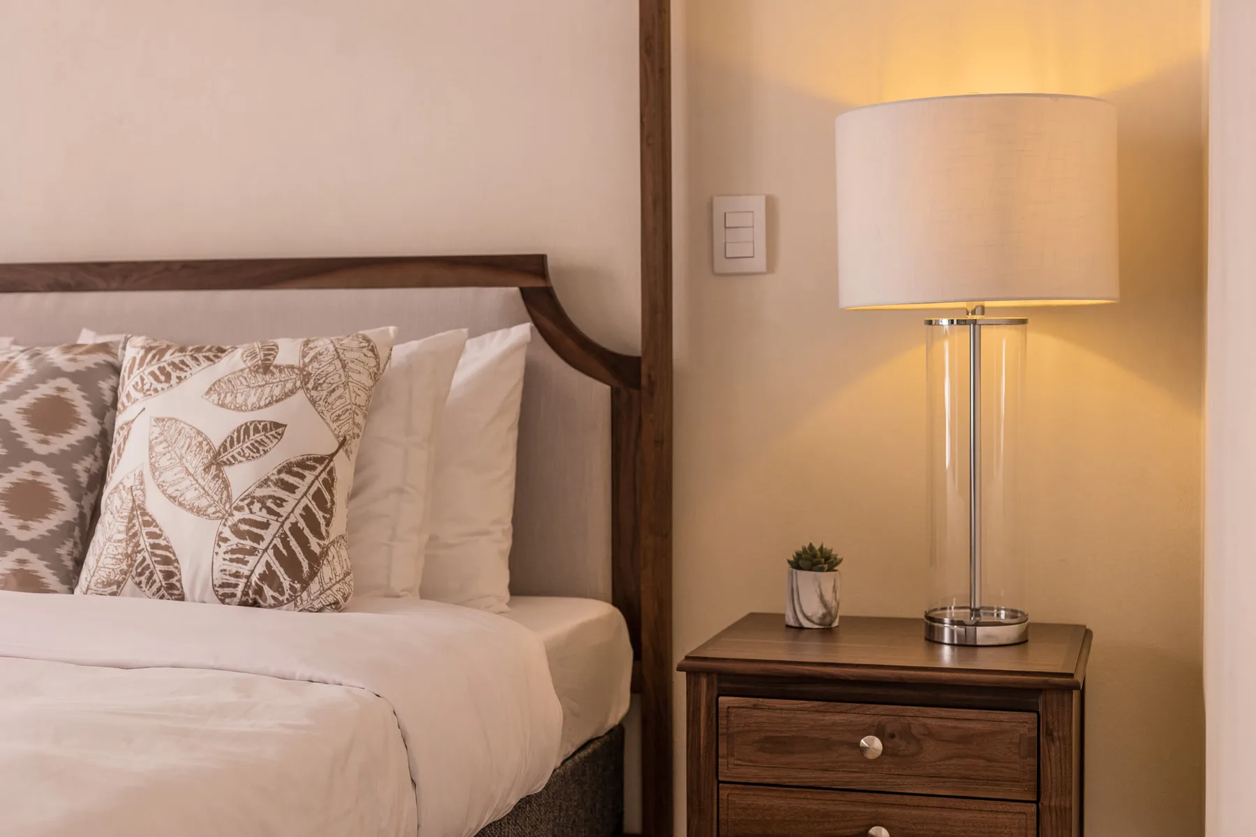 Un dormitorio con una cama tendida, cojines estampados y una lámpara de mesita.