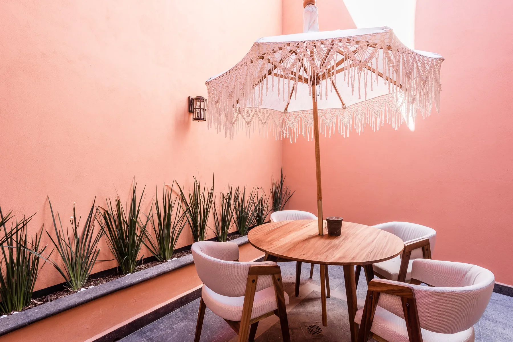Una zona de estar en un patio, con una mesa redonda bajo una sombrilla con flecos.