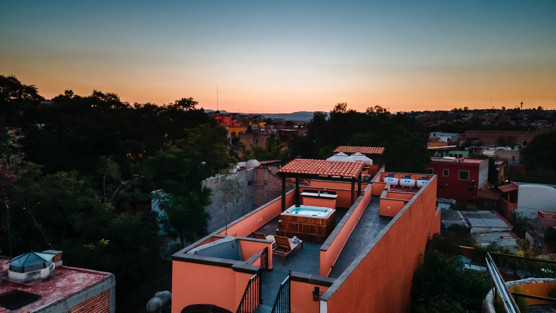 Vista aérea de un edificio de techo plano y viviendas cercanas al atardecer.