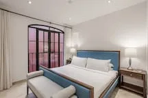 A bedroom with a bed beside tall windows and bedside lamps.