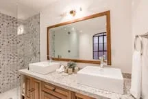 Un lavabo de baño con dos fregaderos está bajo un gran espejo enmarcado.