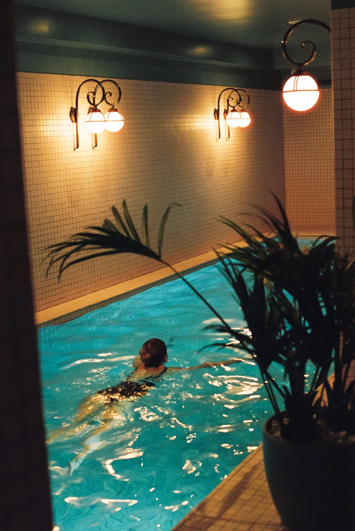 Espacio representativo del hotel: Una piscina cubierta con luces cálidas en la pared y una persona nadando.