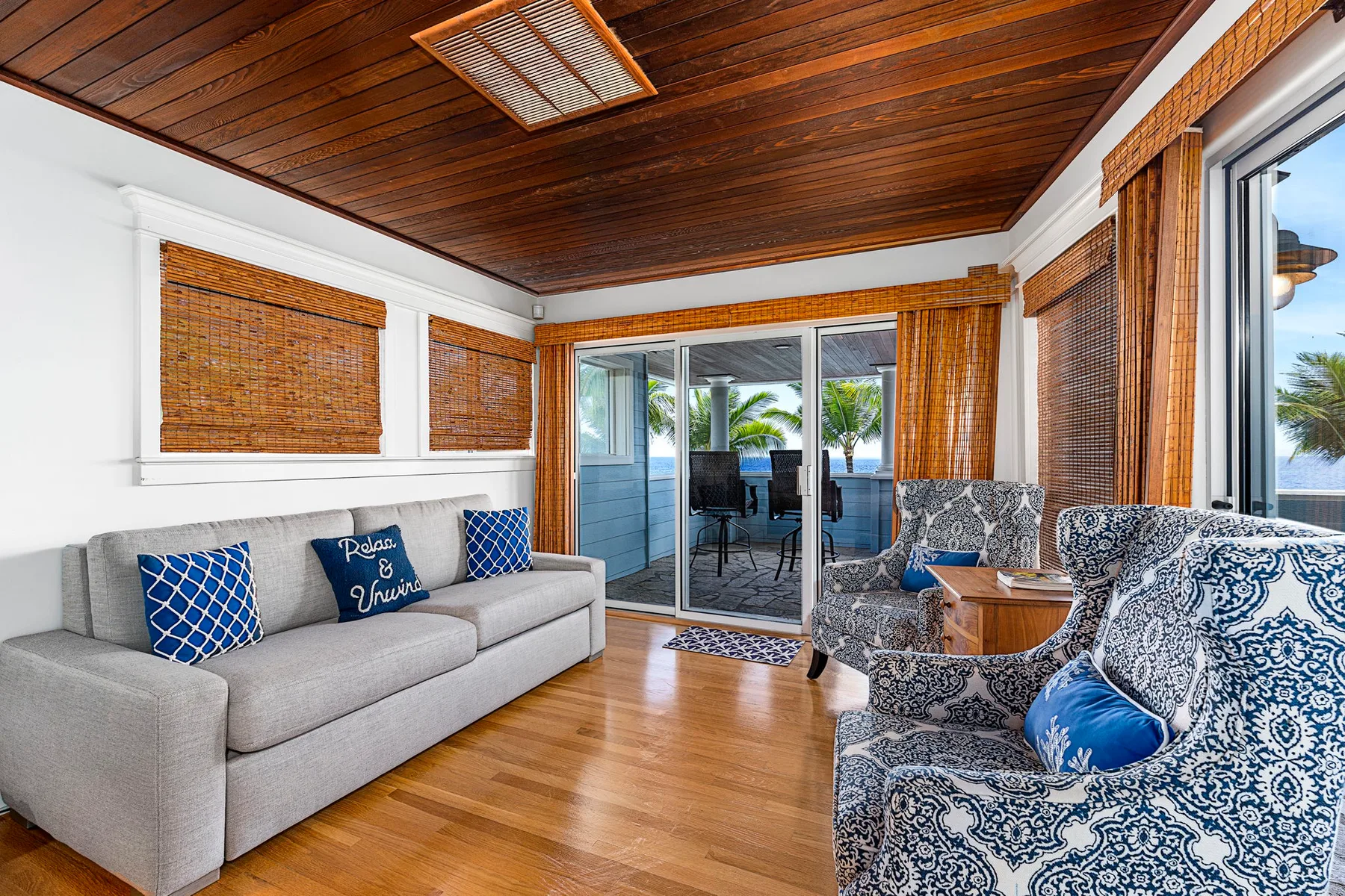 A bright living room with a gray sofa and patterned seating beside glass doors.