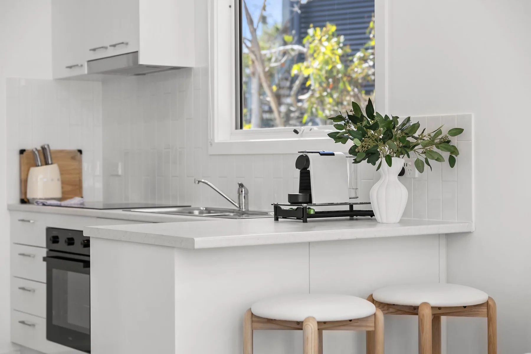 A bright white kitchen with a countertop, small appliance, and two stools.