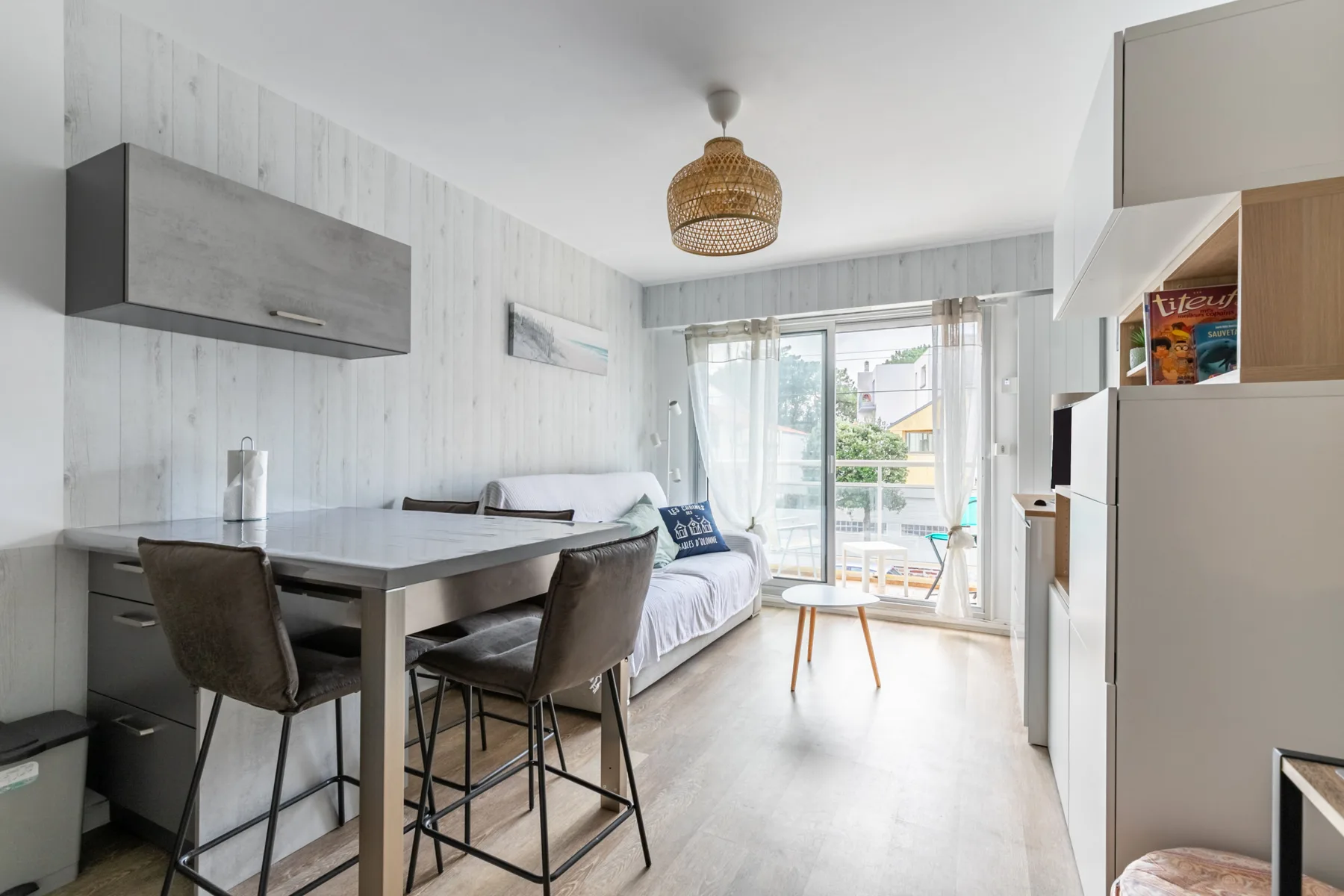 A bright studio living area with a dining table and seating beside glass doors.