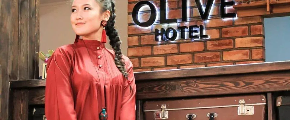 Espacio representativo del hotel: Una mujer está junto a un mostrador de madera bajo un letrero de hotel.