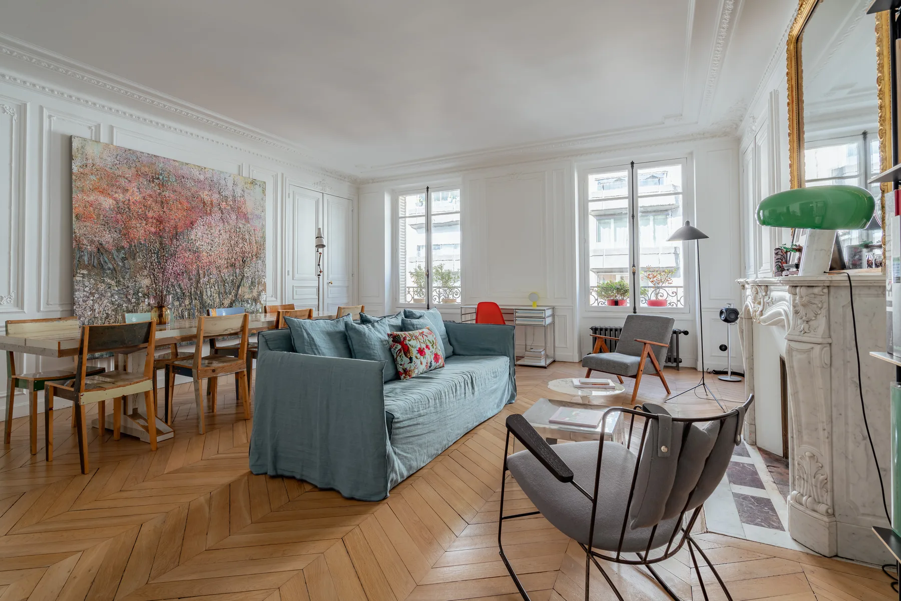 A bright living room with a blue sofa, dining table, and large windows.